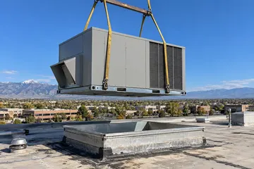 A new rooftop unit lifted by crane onto a roof curb